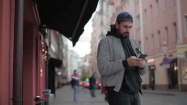 Genç, modern yakışıklı adam küçük bir kasabanın caddesinde telefonla konuşuyor.