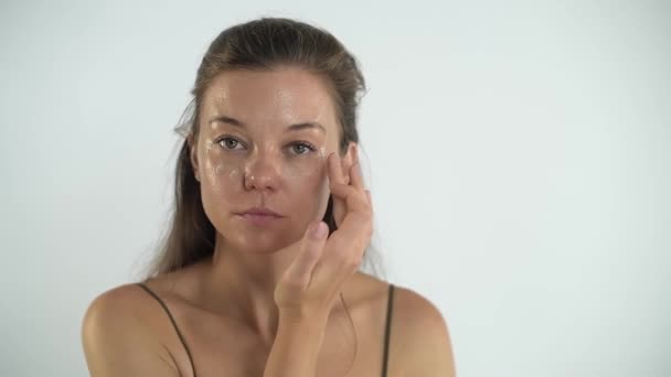 Giovane bella ragazza applica la crema sulla pelle del viso. Massaggio facciale. — Video Stock