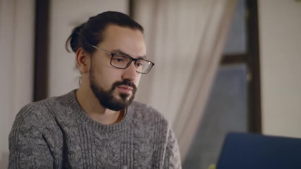 Un hombre joven y guapo con gafas trabaja en un portátil. — Vídeos de Stock