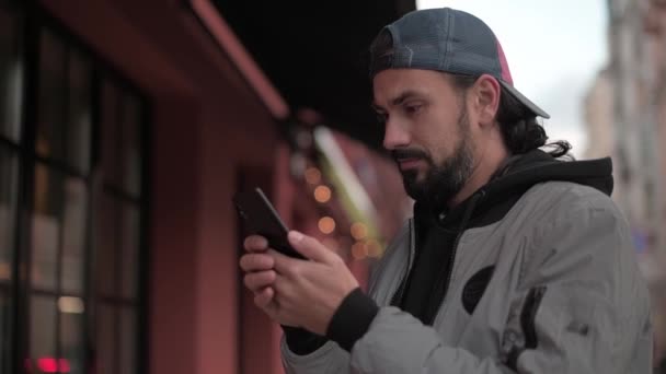 Homem bonito novo com um telefone, em uma rua da cidade em um dia ensolarado do outono. — Vídeo de Stock