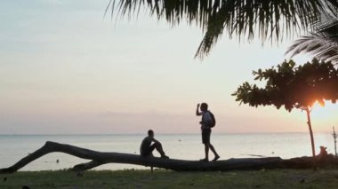 Denizin arka planında batan güneşin ışığında insanların silueti..