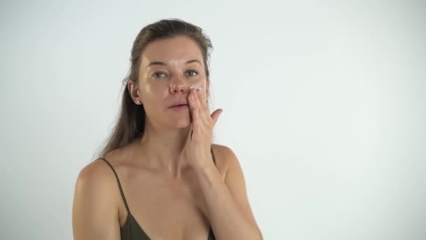 Joven chica bonita aplica crema en la piel de la cara. Masaje facial. — Vídeos de Stock