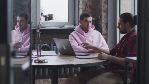 Молодий бізнесмен з ноутбуком розмовляє з колегою, в офісі — стокове відео