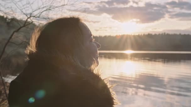 Ein junges, molliges, schönes Mädchen bei Sonnenuntergang am See in den Strahlen der Sonne — Stockvideo
