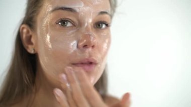 Genç ve güzel bir kız yüz derisine krem sürüyor..
