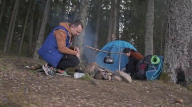 Ormandaki turistler. Adam ateşi yakıyor. Kız çadır kurmuş..