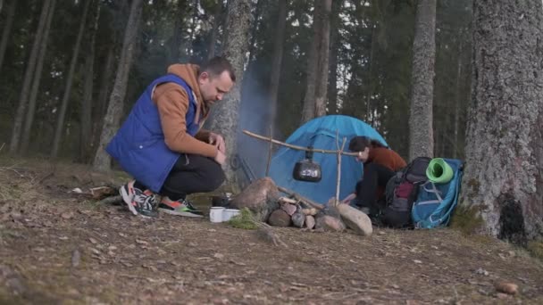 Turistas en el bosque. El hombre enciende el fuego. La chica pone una tienda de campaña. — Vídeos de Stock