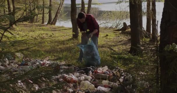 Un voluntario masculino recoge basura esparcida en el bosque en una bolsa de plástico. — Vídeos de Stock