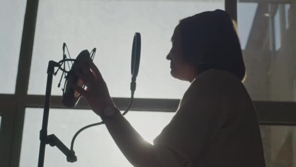 Девушка эмоционально поет в микрофон на заднем плане окна — стоковое видео
