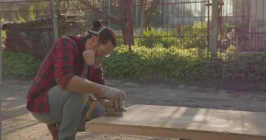 Solunum cihazlı, gözlüklü, parke tahtasını zımpara makinesiyle cilalayan bir adam..