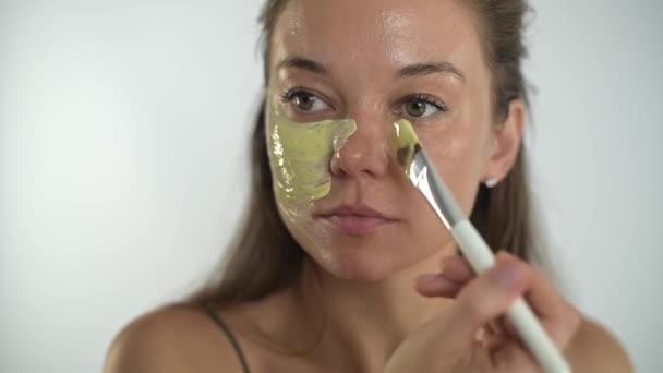 Ein junges schönes Mädchen trägt mit einem Pinsel eine feuchtigkeitsspendende Maske auf ihr Gesicht auf. — Stockvideo