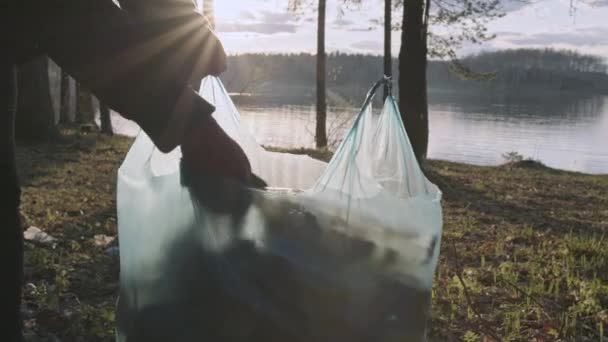 Kamerafahrt, Nahaufnahme von Hand beim Müllsammeln im Wald am See. — Stockvideo