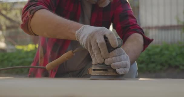 A man in a respirator, goggles, polishes a parquet board with an orbital sander. — Stock Video