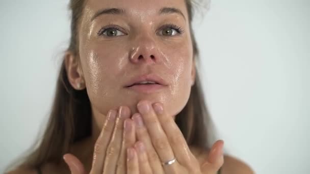 Een jong mooi meisje brengt een transparante hydraterende masker op haar gezicht. — Stockvideo