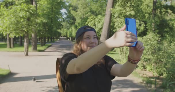 Una chica joven y bastante gordita toma una selfie en el teléfono mientras viaja a pie. — Vídeos de Stock