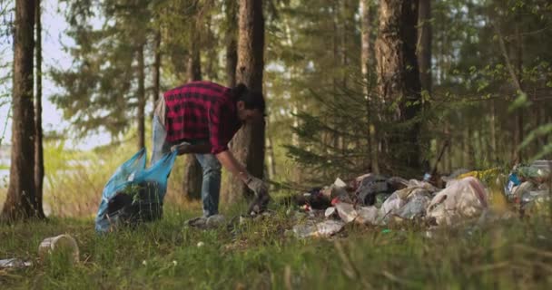 Samec dobrovolník sbírá odpadky roztroušené v lese v igelitovém sáčku. — Stock video