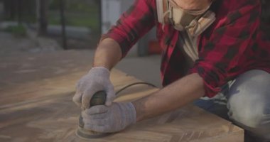 Solunum cihazlı, gözlüklü, parke tahtasını zımpara makinesiyle cilalayan bir adam..