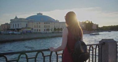 Sundress giymiş genç bir kız nehir kıyısında yürür.