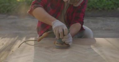 Solunum cihazlı, gözlüklü, parke tahtasını zımpara makinesiyle cilalayan bir adam..