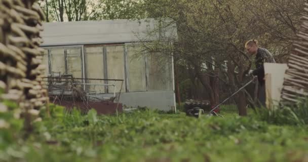 Herbe verte dans le jardin et l'homme avec une tondeuse à gazon au ralenti passe par — Video