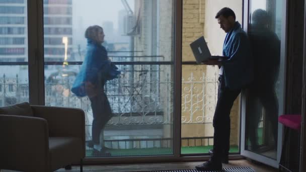 Un ragazzo è in piedi sul balcone con un computer portatile. Una donna si avvicina all'uomo — Video Stock