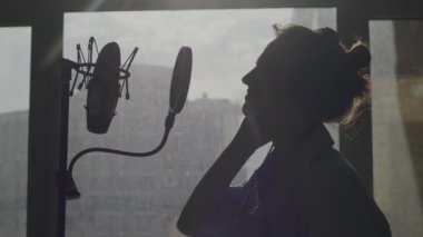 Genç bir kız duygusal olarak arka plandaki mikrofona şarkı söylüyor.