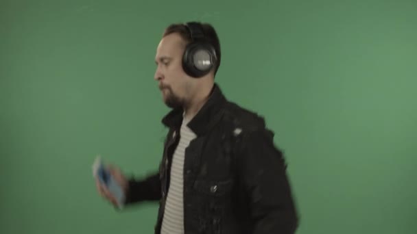 Joven hombre guapo con auriculares bailando en el fondo de una pantalla verde. — Vídeo de stock