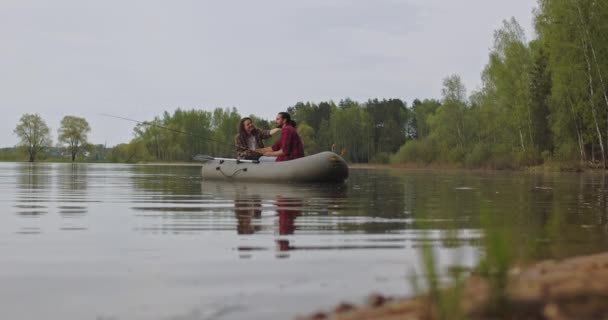 Los pescadores jóvenes en un barco inflable en el lago están pescando. Fotografía cinematográfica. — Vídeo de stock
