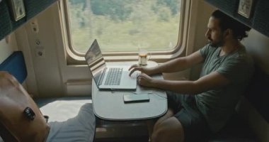 Genç beyaz bir adam trenle seyahat ederken kulaklıkla oturur..