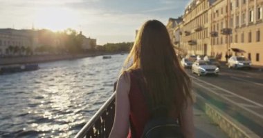 Sundress giymiş genç bir kız nehir kıyısında yürür.