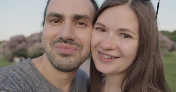 Un jeune beau couple de touristes avec bretelles faire des selfies dans le parc. — Video
