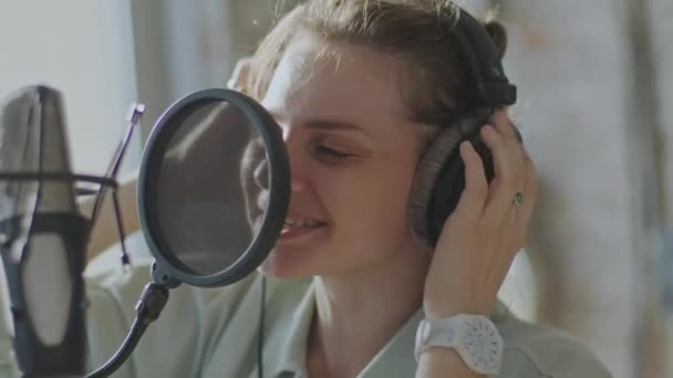 En ung flicka sjunger känslomässigt i en mikrofon i bakgrunden av fönstret — Stockvideo