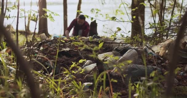 Een mannelijke vrijwilliger verzamelt afval verspreid in het bos in een plastic zak. — Stockvideo