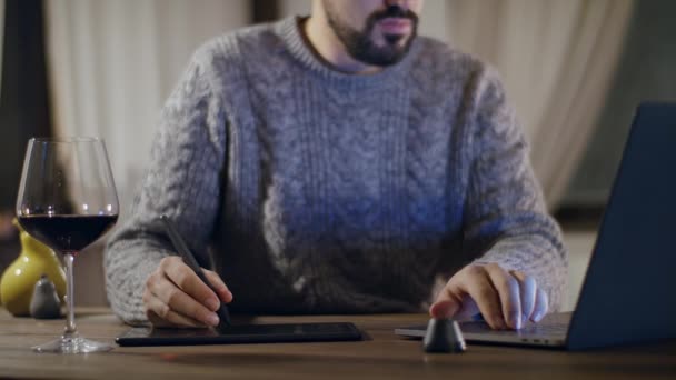 Genç, yakışıklı, sakallı bir adam bir bardak şarapla dizüstü bilgisayarda çalışıyor.. — Stok video