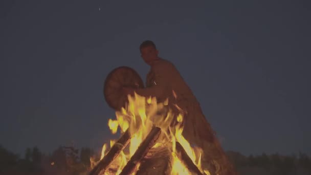 Un chaman avec un tambour saute autour du feu en vêtements pour la cérémonie. — Video