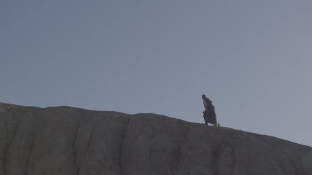 Een vermoeide reiziger in een regenjas wandelt op een zwoele dag over de bergkam — Stockvideo