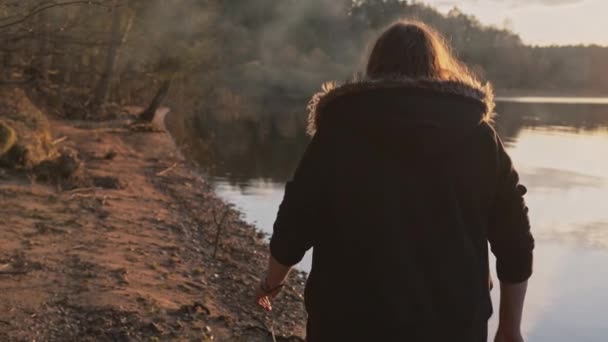 Seorang wanita berjalan di sepanjang tepi sungai pada hari musim gugur yang dingin di matahari musim gugur yang hangat. — Stok Video