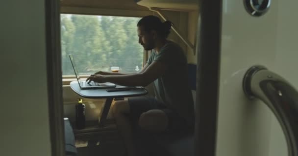 Un giovane caucasico si siede in cuffia con un computer portatile mentre viaggia in treno. — Video Stock