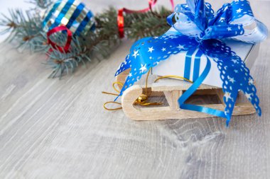 Büyük mavi bir yayı olan bir Noel hediyesi ahşap bir kızağın üzerinde yatıyor. Mutlu yıllar ve mutlu Noeller. Noel tebrik kartı..