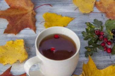 Sonbahar arkaplanı, bir fincan çay, böğürtlen ve sarı yapraklarla boyanmış ahşap bir yüzey. Bir kartpostal veya afiş için sonbahar kompozisyonu.