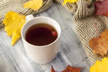 Sonbahar arkaplanı, bir fincan çay, böğürtlen ve sarı yapraklarla boyanmış ahşap bir yüzey. Bir kartpostal veya afiş için sonbahar kompozisyonu.