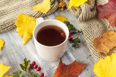 Sonbahar arkaplanı, bir fincan çay, böğürtlen ve sarı yapraklarla boyanmış ahşap bir yüzey. Bir kartpostal veya afiş için sonbahar kompozisyonu. 