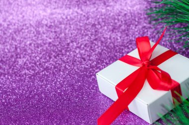 Kırmızı kurdeleli beyaz Noel hediyesi. Mor arka planda Noel ağacının altında bir hediye. Noel ve yeni yıl.