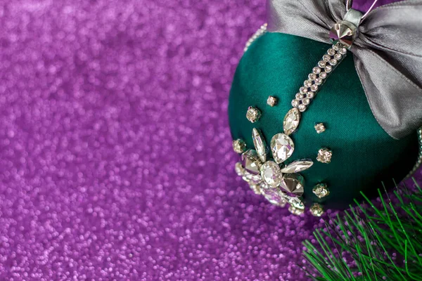 Green Christmas ball in rhinestones for decorating the Christmas tree. Christmas toy. Christmas toy for decorating a Christmas tree on a lilac background. Shining crystals on a green ball. Christmas and new year.