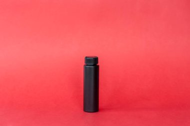 Kırmızı arka planda kremalı siyah şişe. Cilt bakımı, nemlendirici, besleyici ya da güneş kremi. Kozmetik güzellik ürünleri endüstrisi.