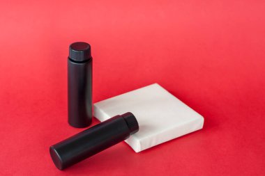 Beyaz bir stantta siyah krema şişeleri. Kırmızı arka planda siyah şişeler. Cilt bakımı, nemlendirici, besleyici ya da güneş kremi. Kozmetik güzellik ürünleri endüstrisi.   