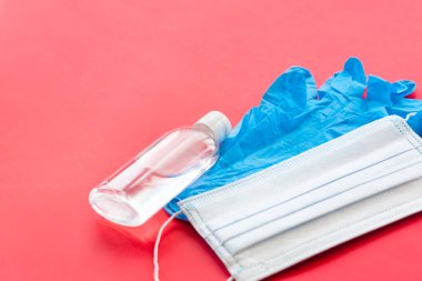 Eldivenli tıbbi maske ve kırmızı arka planda el dezenfektanı. Grip virüslerine karşı korunmak için cerrahi maskeler, koronavirüs, COVID-19. Tıbbi. 