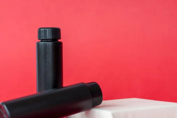 Beyaz bir stantta siyah krema şişeleri. Kırmızı arka planda siyah şişeler. Cilt bakımı, nemlendirici, besleyici ya da güneş kremi. Kozmetik güzellik ürünleri endüstrisi.
