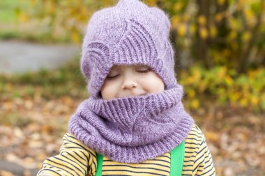 Mor şapkalı ve atkılı bir çocuk. Sonbahar ağaçlarının arka planında bir çocuğun portresi. 