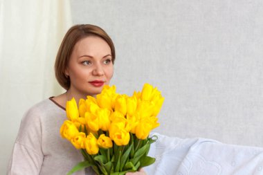 Genç ve güzel bir kızın portresi. Bir kız ve büyük bir buket taze sarı lale. Bahar ve tatil konsepti, 8 Mart, Uluslararası Kadınlar Günü, doğum günü. 